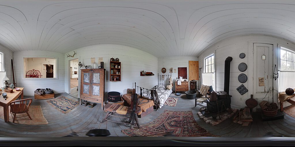 Panoramic view of Stagehand room with small bed, table, wash pitcher, and cabinet.