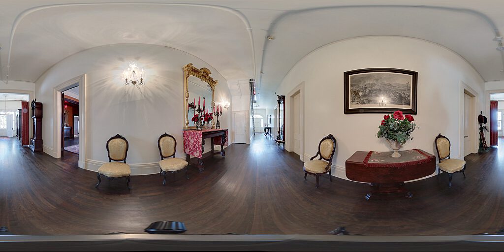Panoramic view of entrance hallway with  carpeted staircase, side table and mirror and chairs.