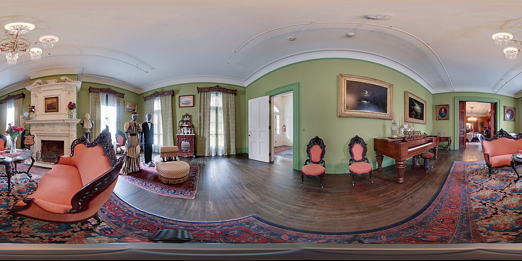 Panoramic view of the Parlor with two mannequins dressed in Victorian Era attire, a tete-a-tete and sofa