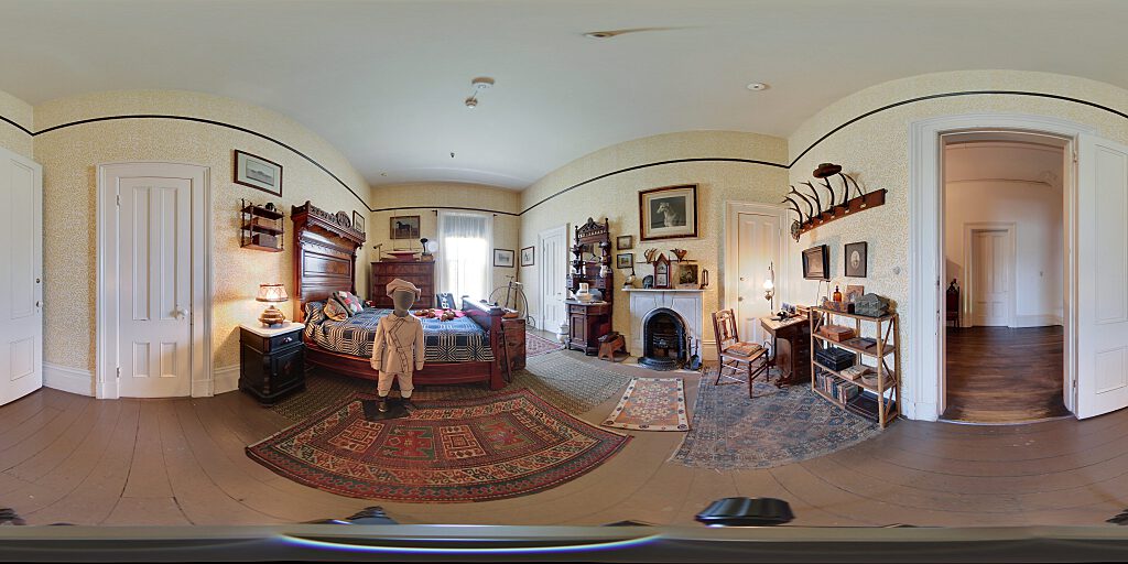 Panoramic view of the boy's room with small male mannequin, bed, fireplace, side table and hat rack made of horns.