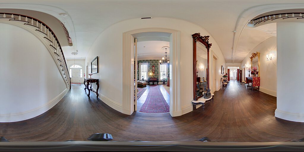 Panoramic view of entrance hallway with  carpeted staircase, side table and painting.