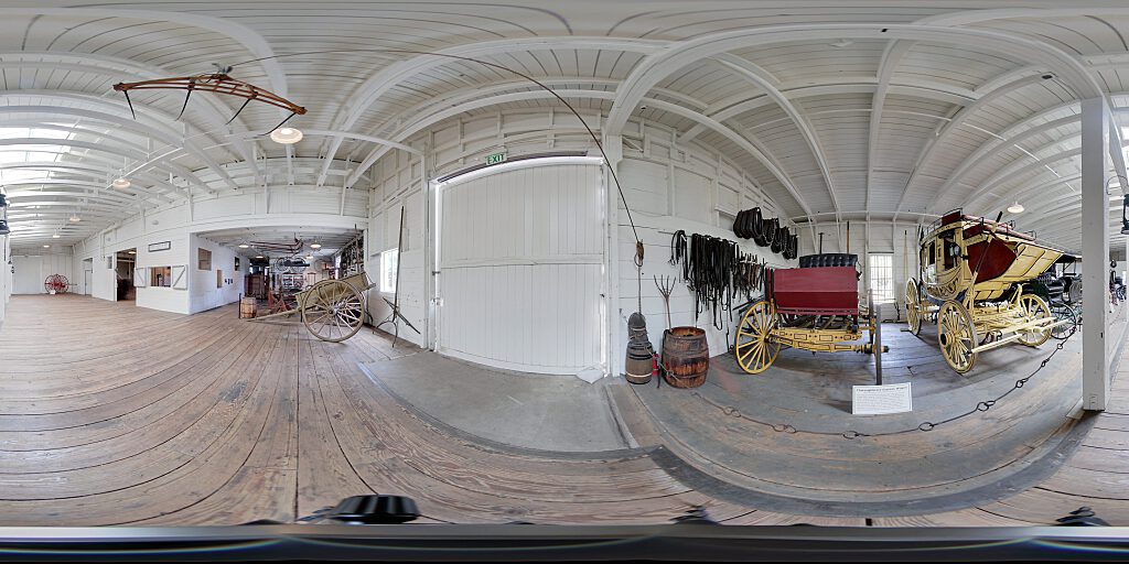 Panoramic view of Barn interior with carriages and concourse.