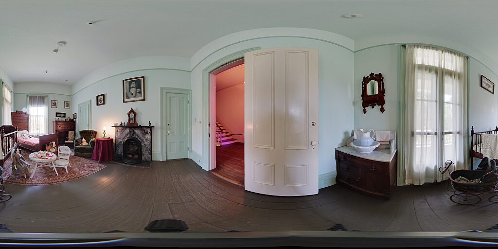 Panoramic view of Nursery entrance with crib, table and chairs, small bed and side table.