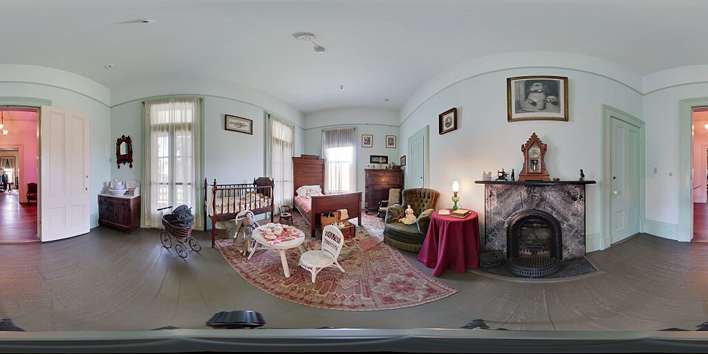Panoramic view of Nursery entrance with crib, table and chairs, small bed and side table.