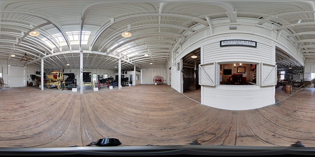 Panoramic view of Barn interior with carriages, concourse and stage coach office.