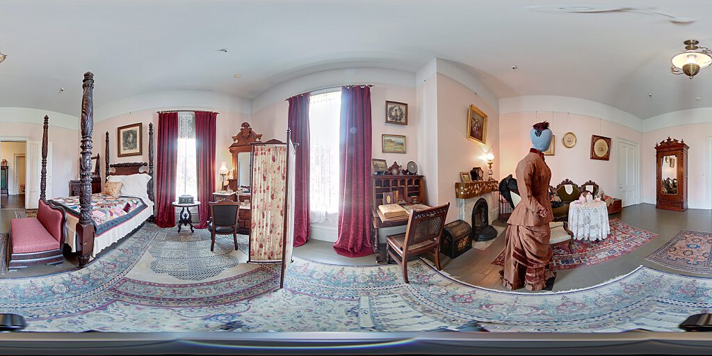 Panoramic view of Mary's Room with four-poster pineapple bed, armoire and side table and carpet. Also sitting area with table and female mannequin.