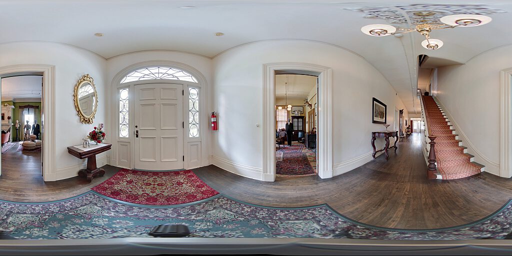 Panoramic view of entrance hallway with  carpeted staircase, side table and mirror.
