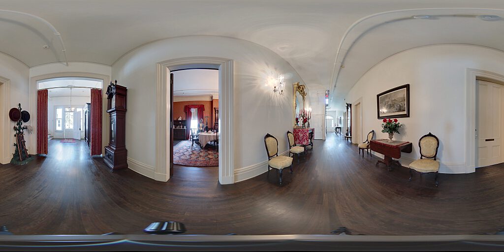 Panoramic view of entrance hallway with  carpeted staircase, side table and mirror and chairs.