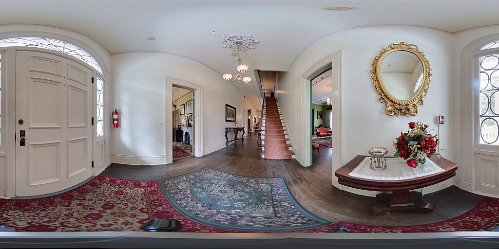 Panoramic view of entrance hallway with  carpeted staircase, side table and mirror.