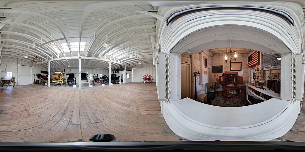 Panoramic view of carriages and interior of stage coach stop interior with table and mail pieces and American flag.