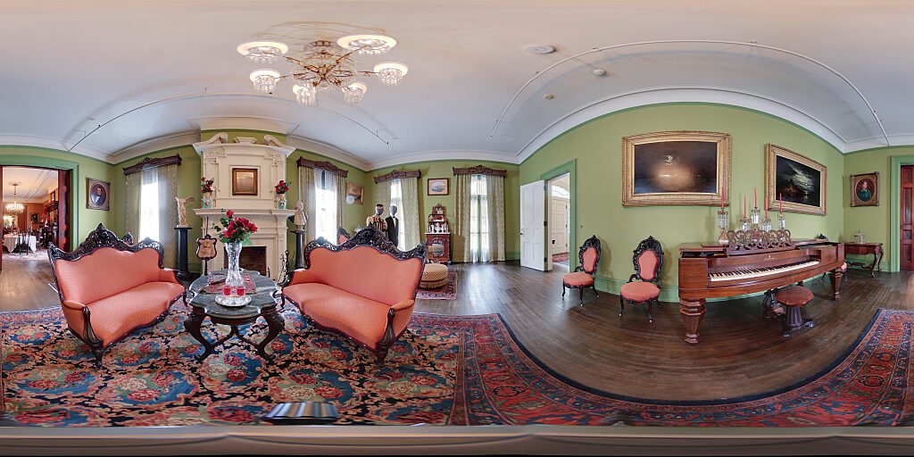 Panoramic view of Parlor with fireplace, male and female mannequines in Victorian dress, a George Washington bust and Victorian Era furniture and piano