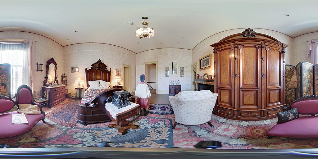 Panoramic view of the girl's room with small female mannequin, double bed, side table, pitcher, armoire and fireplace.