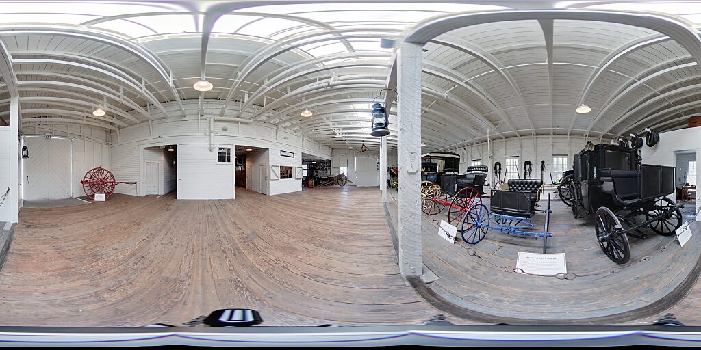 Panoramic view of Barn interior with carriages and concourse.