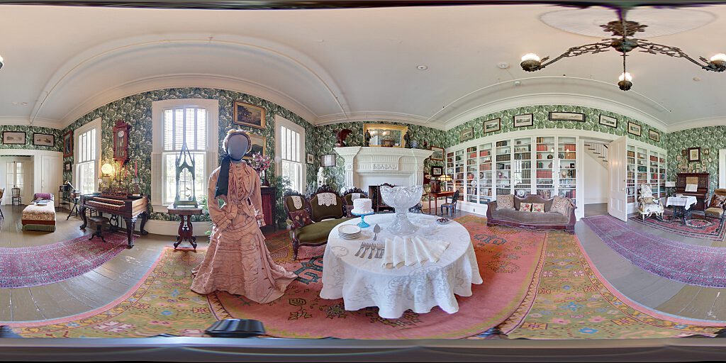 Panoramic view of Family Room with sofa, steer horn chair, table and closeup of female mannequin in period attire